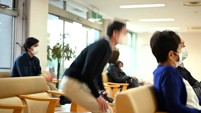 マスクをした人々が病院のロビーに座っている。
呼び出しをうけて男性が受付に向かう。