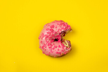 Flatly of a bitten dough on yellow background. Bitten pink donut with sprinkles isolated.