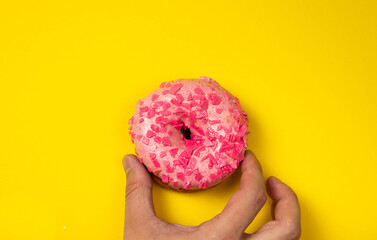 Hand hold pink donut with sprinkles on yellow background.