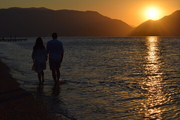 Fototapeta premium Silhouettes of girls and boys holding hands against the background of the sunrise in the sea. Sunrise in Icmeler.