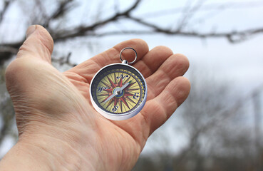Old classic navigation compass in hand on natural background as symbol of tourism with compass,...