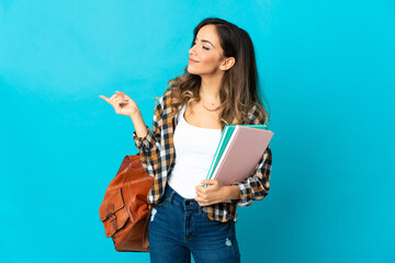 Young student woman isolated on blue background pointing finger to the side