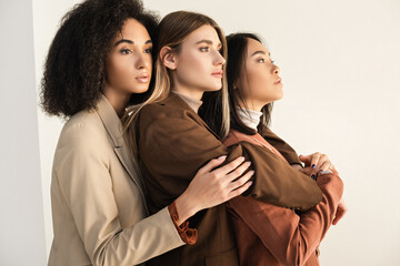 young and stylish interracial models in suits hugging while posing on white