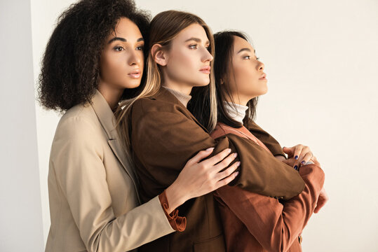 young and stylish interracial models in suits hugging while posing on white