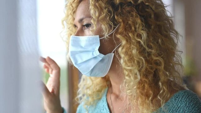 portrait and close up of one young curly woman wearing at home looking at the window of her house in quarantine - lockdown lifestyle for the covid-19
