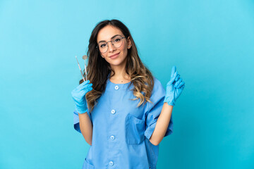 Woman dentist holding tools over isolated on blue background showing and lifting a finger in sign...