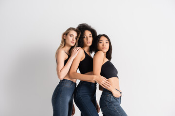 Fototapeta premium interracial women in tops and denim jeans posing on white