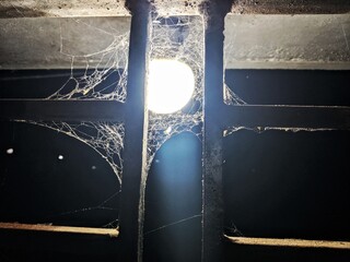 A very old and dirty house close up of spider net and dirt near a bulb or light souce-a vertical photo