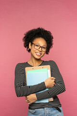 Young happy Afro-American tutor or teacher woman isolated on pink studio wall. Student girl wear...