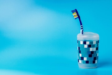 Toothbrush in a plastic cup isolated on a blue background. Oral hygiene and care concept