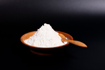 A pile of white wheat flour in a Cup. Wooden spoon.