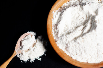 Brown Cup with white flour. Wooden spoon nearby. A handful of ingredient is on the table.