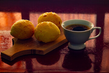 Xícara branca de café e pães de queijo sobre superfície reflexiva.