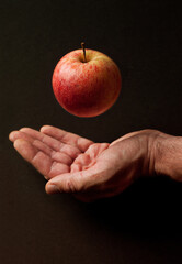 Hand with red apple hovering in front of dark background