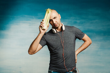 Funny bald man in headphones on his neck put celery to the head (on a blue background)