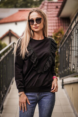 Young blond-haired fashion model takes photos for a fashion store outdoors with a blurred background.