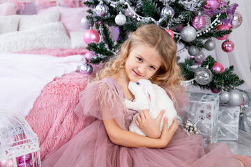 baby girl with rabbit at the Christmas tree in a beautiful pink dress, new year and Christmas concept