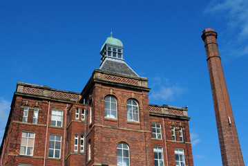 Fototapeta na wymiar Old Victorian Mill Building & Tall Industrial Chimney against Blue Sky 