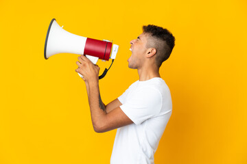 Young brazilian man isolated on yellow background shouting through a megaphone to announce something in lateral position