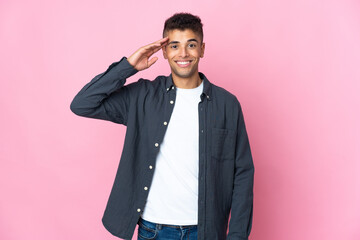 Young Brazilian man isolated on pink background saluting with hand with happy expression