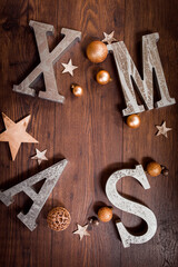 Silberne XMAS Buchstaben in warmen gold- und braun Tönen auf Holz mit goldenen Weihnachtskugeln und Sterne aus Holz