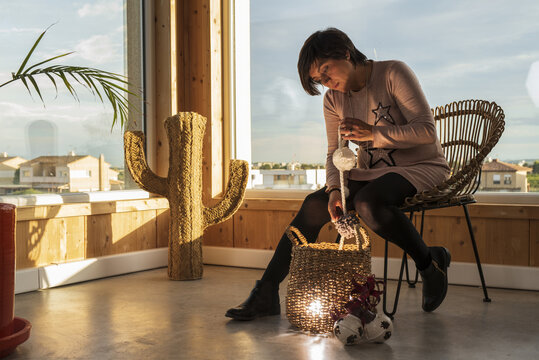 Adult Female Sitting On A Chair And Pulling Out Christmas Decorations From A Basket