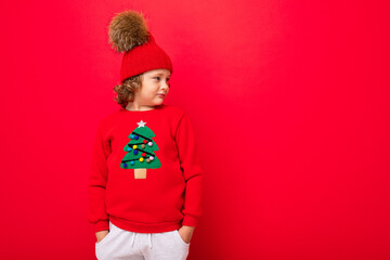 cool teenager in a red Christmas sweater fooling around against the background of a red wall, a...