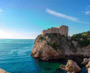 Fototapeta na wymiar Dubrovnik's Fortica castle on the peak of a peninsula, seen while walking on the old city walls of Dubrovnik. Standing high surrounded by the blue adriatic sea