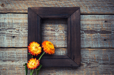 Fototapeta na wymiar Old wooden frame with autumn flowers and leaves on brown rustic wooden background. Autumn composition with copy space.