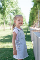 little girl blonde 5 years old in denim sarafan walks around the park.