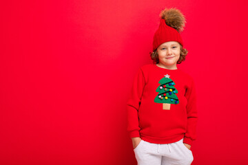 cheerful funny boy on a red background in a warm hat and sweater with a Christmas tree