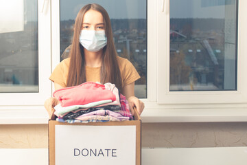 Young woman volunteer with a box of clothes for the poor, orphans, needy children and homeless...