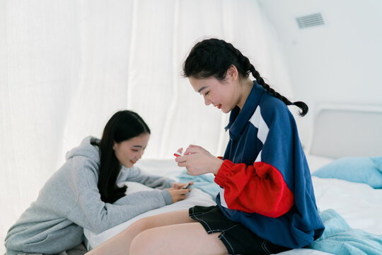 two young fashion asian female friends using cell phone on bed