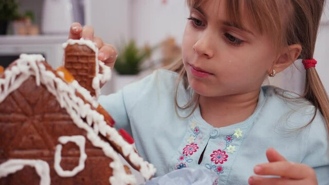 Little girl in the kitchen icing a gingerbread cookie house - close up, camera slide
