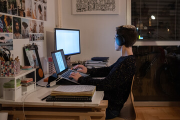 Young Short-Haired Woman With Headphones Sitting At The Desk And Using Laptop Late At Night