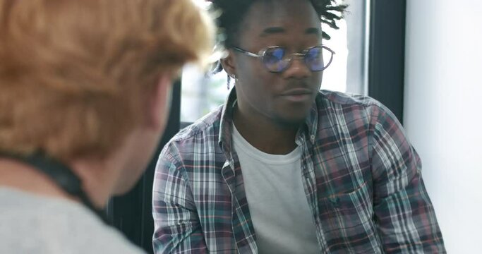 Confident African American man in eyeglasses talking with colleagues or friends in sunny office. Portrait of handsome positive guy chatting with coworkers or mates in sunlight. Cinema 4k ProRes HQ.