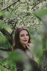 Portrait of a beautiful smiling brunette under blooming tree branches in the garden. Spring time.