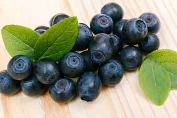 A heap of bilberries on a wooden table. Bilberry leafs. Macro shot.