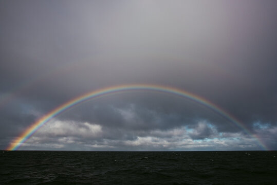 Rainbow in overcast dark sky above ocean