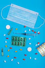 Scattered pills, blisters and a medical mask on a blue background.