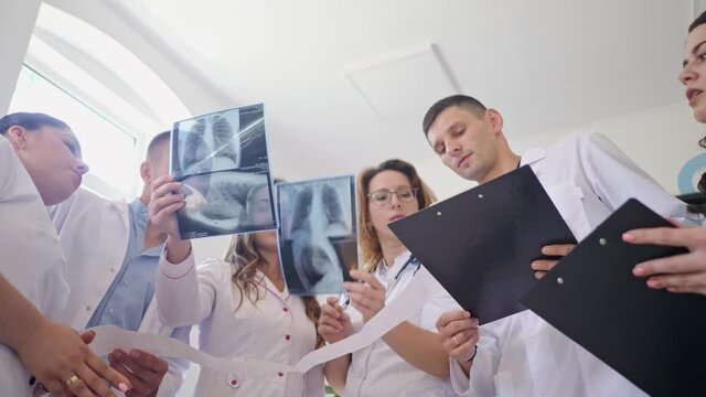 Female Doctor and Young Medical Interns in Medical Clothing Studying Together the Results Chest X-Ray Scan of Patient. Middle-Aged Woman Therapist Teaching Young Interns How to Analyze X-Ray Image