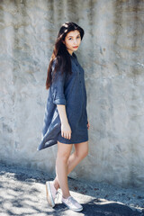 Young stylish girl standing in front of white concrete wall in sunny day. Pretty girl with long dark hair and red lips. 