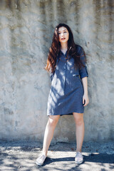 Young stylish girl standing in front of white concrete wall in sunny day. Pretty girl with long dark hair and red lips. 