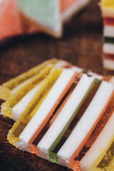 Sliced multicolored striped marmalade on wooden table. Colorful jelly candy close-up. Macro shot, selective focus.