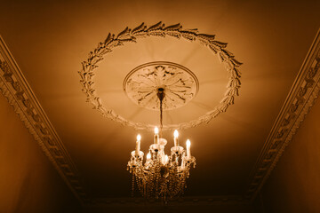 Crystal glowing lustre on ornamental white ceiling in manor
