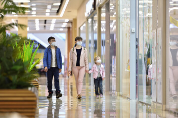 Fototapeta premium Mom, daughter and son in protective masks walk through the mall and look at the shop windows