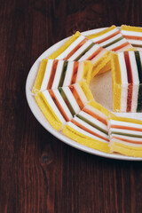 Sliced multicolored striped marmalade in the plate on wooden background. Colorful jelly candy close-up. Macro shot, selective focus.