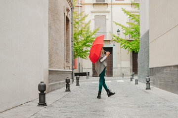 Pretty blonde woman walking down the street with a red umbrella
