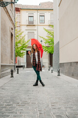 Beautiful blonde woman smiling on the street and looking at the camera with a red umbrella.