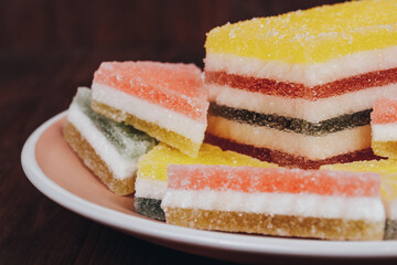 Colorful jelly candy in the plate on wooden background. Multi-colored marmalade jelly candy's. Heap of triangular and rectangular  marmalade candy.
